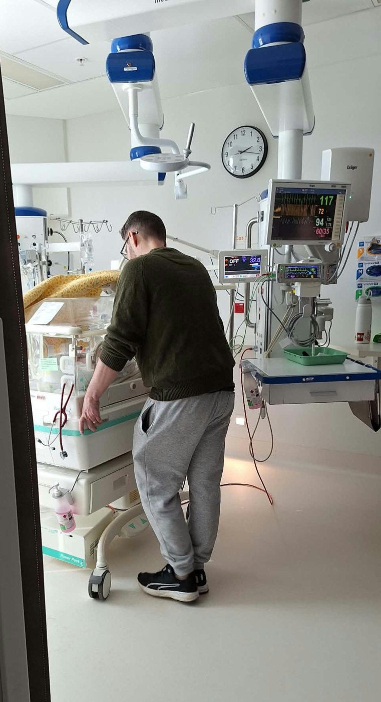 Calum standing at the incubator, watching over his daughter in the NICU